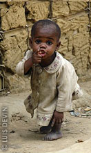 Bambina pigmea davanti a una capanna di fango